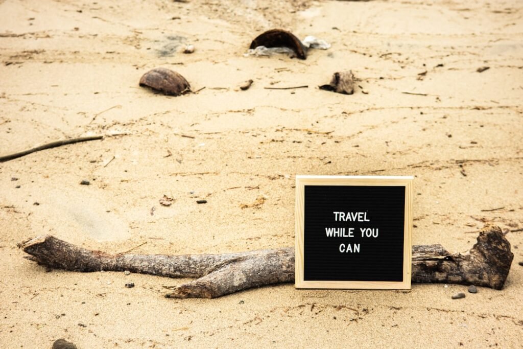 a sign that says travel while you can on a beach