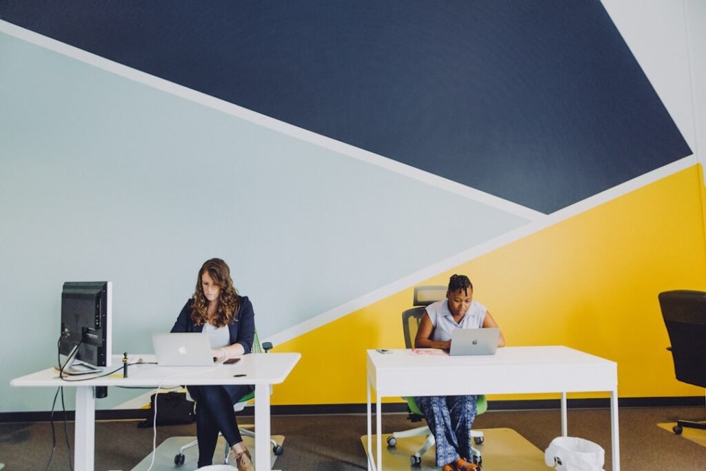 two women sitting beside table using MacBooks